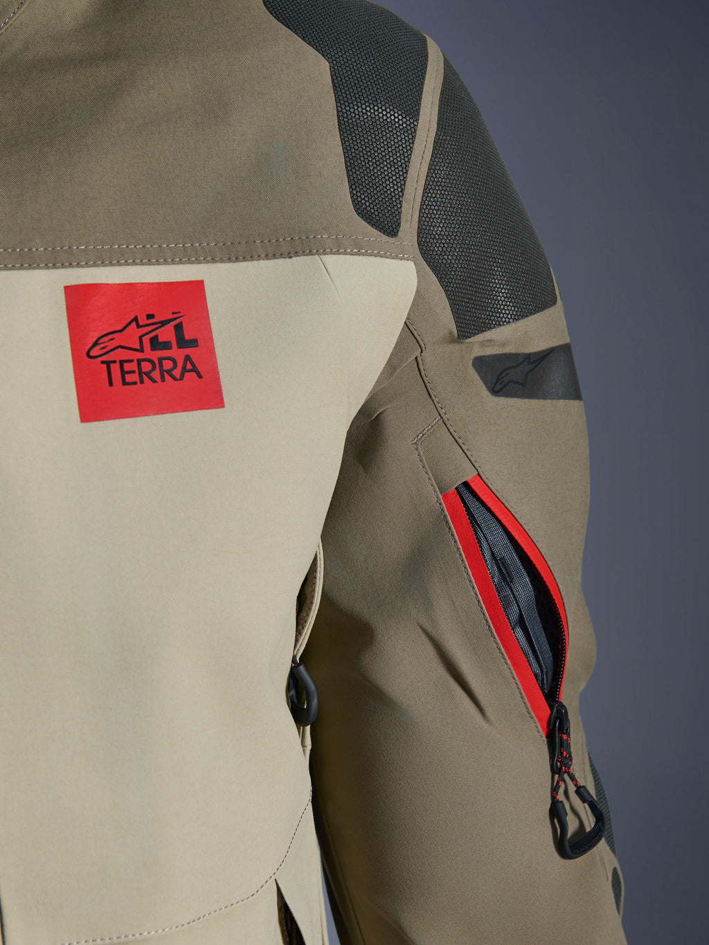 Alpinestars Nazca 3L GORE-TEX PRO Jacke, Walnut Rock Brown, Detailansicht der hinteren Schulter und des Ärmels, roter „ALL TERRA“ Logo-Patch, strukturierte schwarze Superfabric-Schultereinsätze, Belüftungsöffnung am Arm mit Reißverschluss und rotem Besatz, Premium-Abenteuer-Motorradbekleidung.