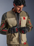 Alpinestars Nazca 3L GORE-TEX PRO Jacke, Walnut Rock Brown, Adventure-Motorradjacke mit offenem Frontreißverschluss und zentralem Mesh-Belüftungspanel, rotes All Terra-Branding, getragen mit schwarzen GORE-TEX-Motorradhandschuhen, technische Ausrüstung für Offroad-Touren