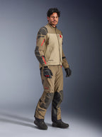 Alpinestars Nazca 3L GORE-TEX PRO Jacke, Walnut Rock Brown, Adventure-Motorradjacke getragen mit passender Hose und schwarzen Handschuhen, mit dunkelgrauen Verstärkungen, roten Reißverschluss-Details und einer hochleistungsfähigen laminierten Außenschicht.
