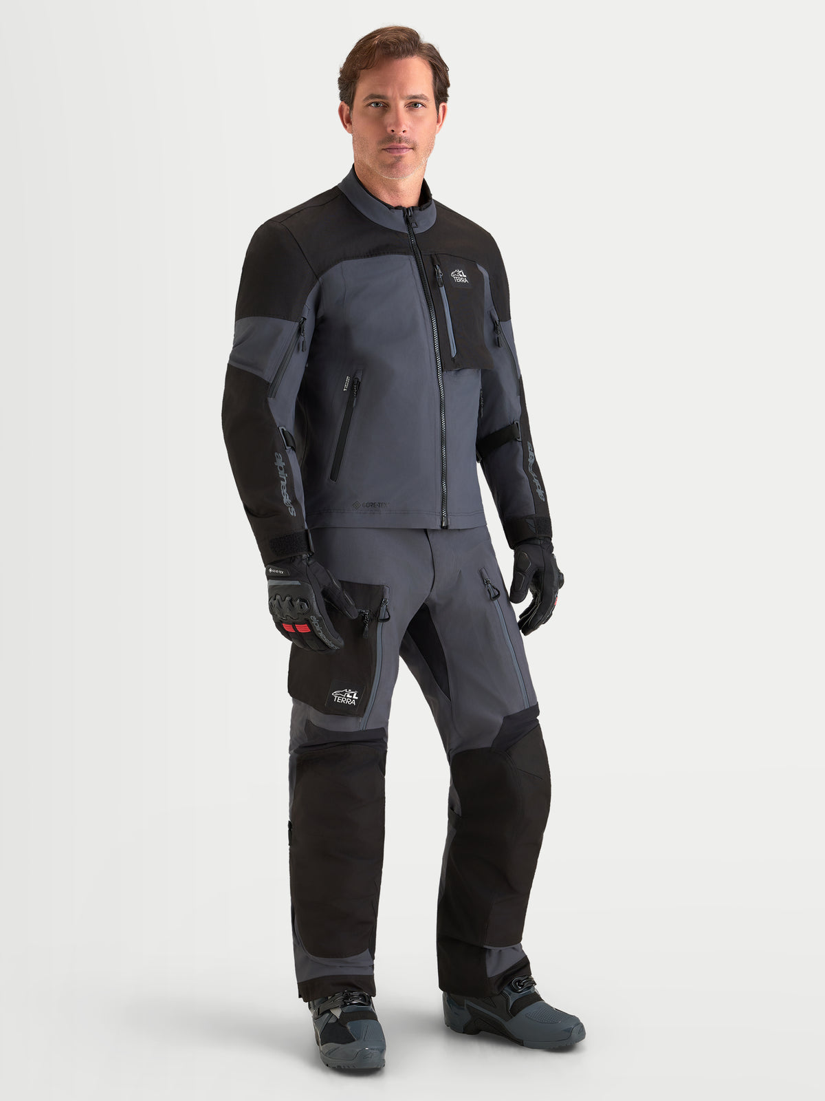 Alpinestars Arenis Gore-Tex Jacke, Herren-Adventure-Motorradjacke in Schwarz und Dunkelgrau, getragen von einem männlichen Model mit passender Ausrüstung, wasserdichte Gore-Tex-Textilkonstruktion