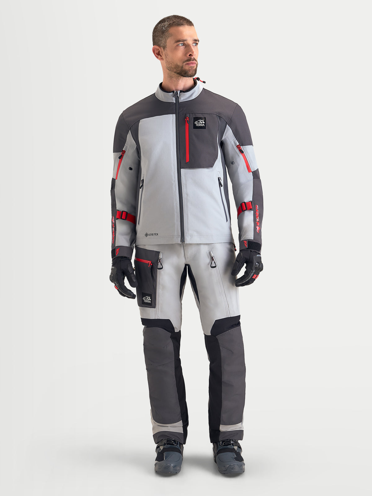 Alpinestars Arenis Gore-Tex Jacke, Herren-Adventure-Motorradjacke in Mittelgrau, Dunkelgrau und Schwarz, Frontansicht im Studio getragen von einem männlichen Model mit wasserdichter Gore-Tex-Konstruktion und roten Reißverschlussdetails