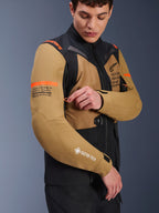 Alpinestars ST-7 2L GORE-TEX Jacke in Gobi-Braun und Schwarz, Adventure-Touring-Motorradjacke, getragen von einem Model, das eine Belüftungsöffnung am Ärmel einstellt, mit orangefarbenen Akzenten, Koordinatengrafiken und GORE-TEX-Logo