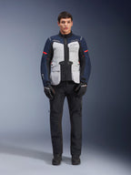 Alpinestars ST-7 2L GORE-TEX Jacke, Adventure-Touren-Motorradjacke, Eisgrau, Dunkelblau und Schwarz, getragen mit schwarzer Hose und Handschuhen, große Cargo-Taschen vorne, rote Akzente an den Ärmeln, laminierte GORE-TEX-Außenschicht für wasserdichte Performance.