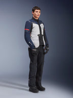 Alpinestars ST-7 2L GORE-TEX Jacke in Ice Gray, Dunkelblau und Schwarz mit roten Akzenten, getragen von einem männlichen Modell mit schwarzer Motorradhose und Handschuhen, professionelle Adventure-Touring-Motorradausrüstung