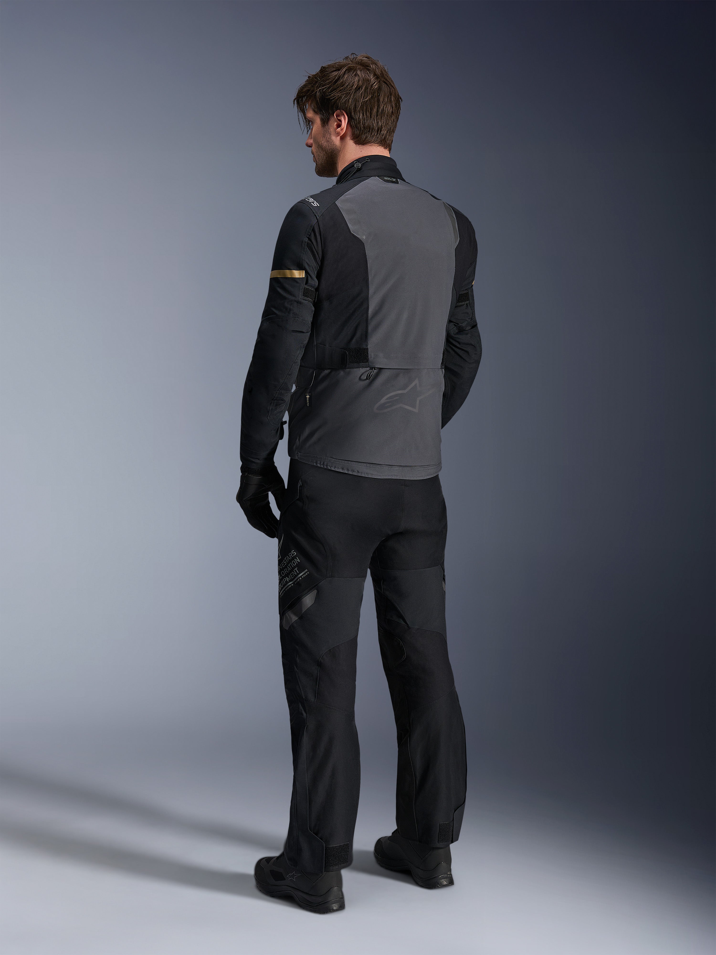 Alpinestars ST-7 2L GORE-TEX Jacke, Dunkelgrau und Schwarz mit Akzenten in Dark Khaki, Rückansicht eines Fahrers, der die Jacke und die passende Motorradhose trägt, Adventure-Touring-Ausrüstung mit wasserdichter laminierter Konstruktion