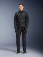 Motorradfahrerin in Alpinestars Damen Stella ST-7 2L GORE-TEX Jacke und Hose, schwarzes Motorrad-Tourenoutfit, wasserdichte und atmungsaktive technische Ausrüstung, mit passenden schwarzen Handschuhen und Stiefeln, Ganzkörper-Schutzausrüstung mit reflektierenden Elementen, modernes technisches Design für Adventure-Riding