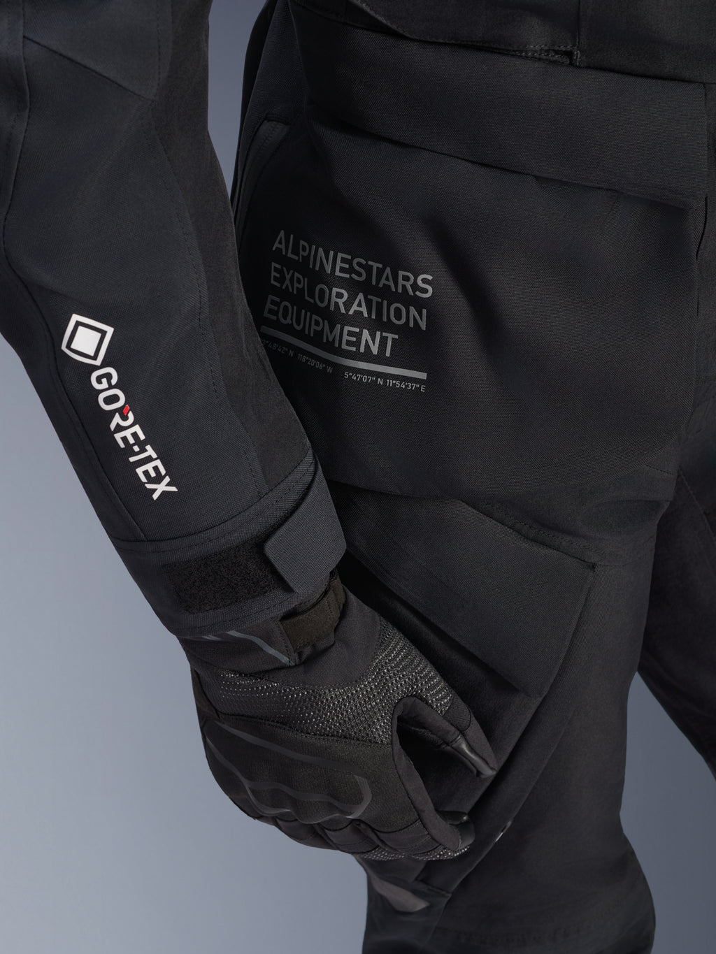 Alpinestars Stella ST-7 2L GORE-TEX Jacke für Damen, schwarze Adventure-Touring-Jacke, Nahaufnahme des Ärmels mit weißem GORE-TEX-Logo, 'Alpinestars Exploration Equipment'-Schriftzug auf der Hüfte, schwarzer Motorradhandschuh, wasserdichtes Textilmaterial mit funktionalen Cargo-Taschen