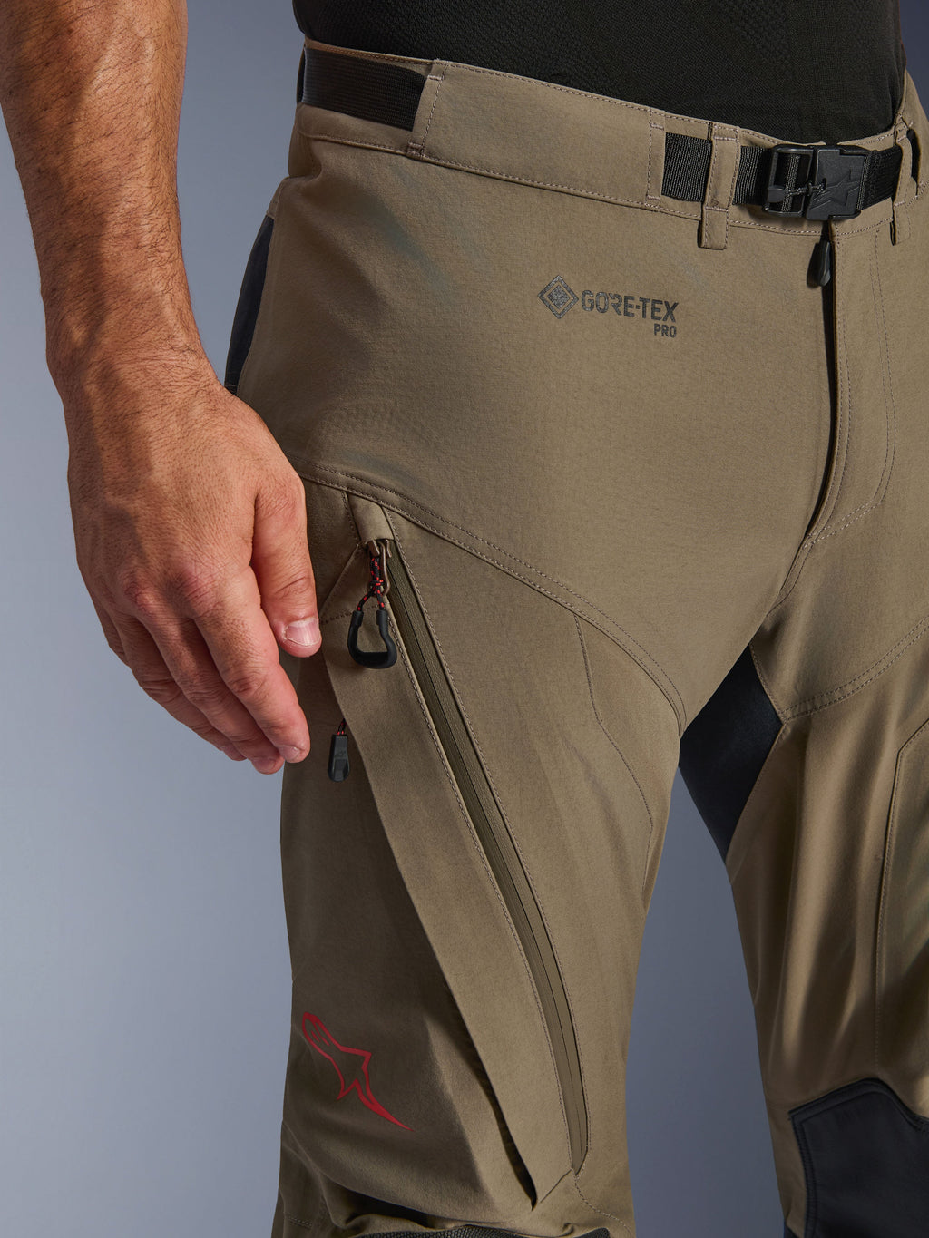 Alpinestars Nazca 3L GORE-TEX PRO Hose, technische Adventure-Motorradhose, Walnut Black, Detailaufnahme von Hüfte und Oberschenkel mit GORE-TEX PRO Branding, diagonaler Reißverschluss-Cargotasche, verstellbarem Taillengürtel mit Schnalle und rotem Stern-Logo.