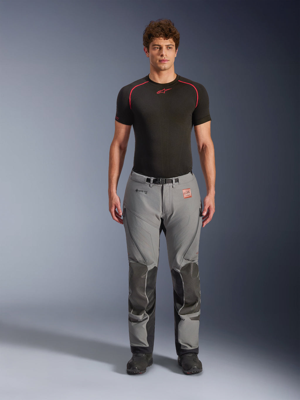Alpinestars Nazca 3L GORE-TEX PRO Hose, Adventure-Motorradhose, Grau und Schwarz, getragen von einem Model mit schwarzem Base Layer, mit verstärkten Knieeinsätzen, GORE-TEX PRO Branding und einem robusten Textildesign für Touren bei jedem Wetter