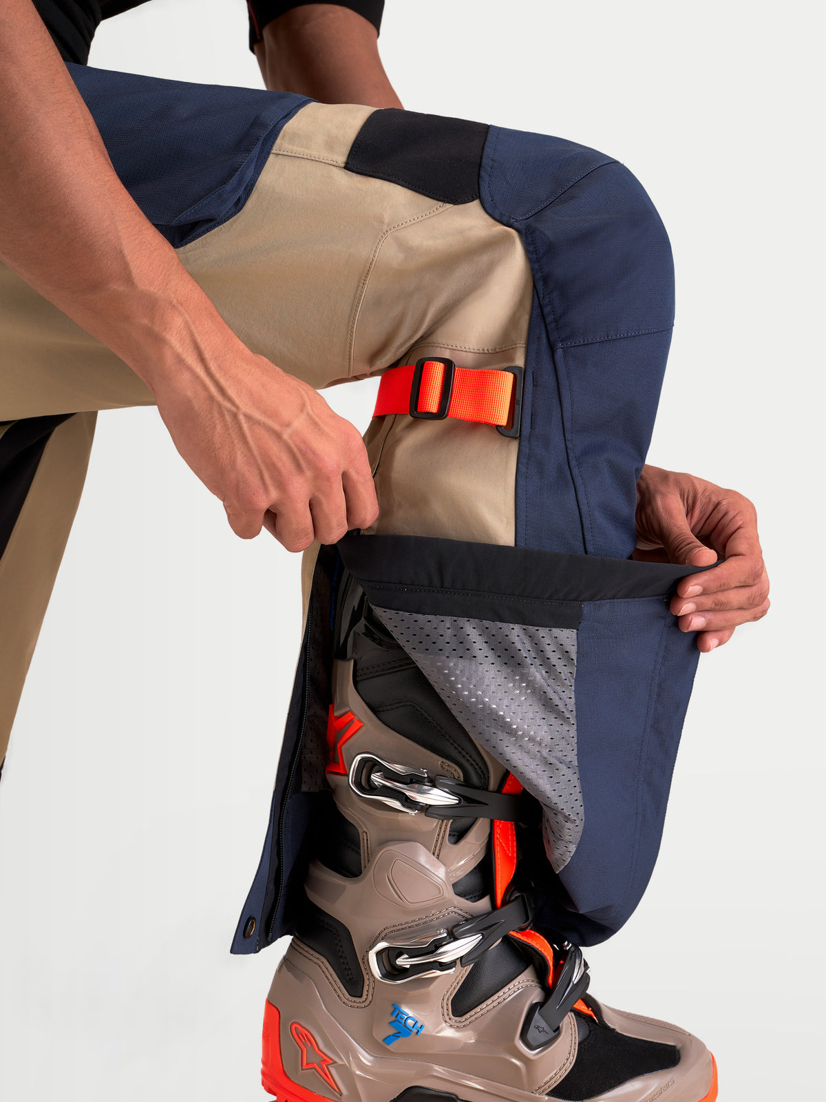 Alpinestars Arenis Gore-Tex Hose, Herren-Abenteuer-Motorradhose in Nachtmarineblau und Aluminium, Nahaufnahme eines Modells beim Einstellen des Unterschenkelreißverschlusses über einem Abenteuerstiefel, wasserdichte Textilkonstruktion.