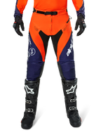 Alpinestars Pro-Dura Hose, Motocross- und Enduro-Hose, Navy, Hot Orange und Weiß, mit schwarzen Einsätzen und weißen Logos, getragen mit schwarzen Offroad-Stiefeln und Handschuhen, professionelle Schutzausrüstung für Trail- und Offroad-Fahrten