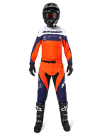 Motocross-Fahrer in Alpinestars Pro-Dura Hose in Navy, Hot Orange und Weiß, mit passendem langärmeligem Trikot, schwarzem Helm mit Goggles, schwarzen Handschuhen und schwarzen Motocross-Stiefeln, komplette Offroad-Rennausrüstung.