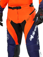 Alpinestars Pro-Dura Hose, Enduro-Motorradhose, Navy, Hot Orange und Weiß, Detailansicht der Taille mit magnetischem SX2-Verschluss und Belüftungsöffnungen mit Reißverschluss an den Oberschenkeln, strapazierfähiges Ripstop-Material mit markantem Branding, getragen mit passender Ausrüstung