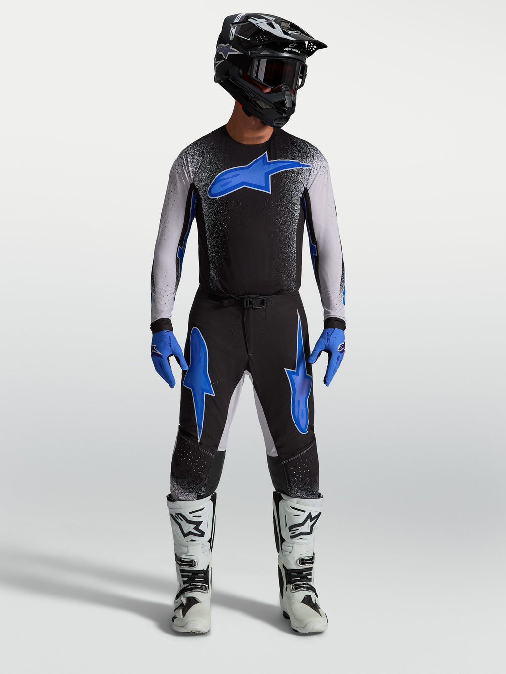 Alpinestars Supertech Hiten AFD Hose, Motocross-Hose für Herren, Schwarz und Blau, am Model mit passendem Trikot und weißen Motorradstiefeln, professionelle Offroad-Rennsport-Ausrüstung
