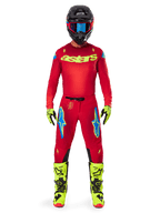 Motocross-Fahrer in kompletter Rennausrüstung, rotes Trikot mit gelbem Fluo-Astars-Logo, Alpinestars 2025 Supertech Maker Hose in Bright Red und Yellow Fluo, mit blauen Logos an den Oberschenkeln, gelbe Fluo-Handschuhe und -Stiefel, schwarzer Helm mit blauer Brille, koordiniertes Motocross-Outfit auf Profi-Niveau
