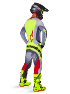 Motocross-Fahrer in einer Dreiviertel-Rückansicht in Alpinestars 2025 Techstar Melt Hose in Leuchtend Rot und Grau, mit einem auffälligen neongelben Logo auf dem Gesäß, passendem grau-neongelbem Trikot, leuchtend neongelben Stiefeln und einem schwarzen Helm mit Neon-Brille, professionelles Offroad-Rennausrüstungs-Set.