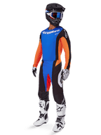 Alpinestars 2025 Techstar Melt Gear Set, Motocross-Fahrer mit blauem Trikot und orangen Ärmeln, schwarze Hose mit blauen und orangen Akzenten, passender schwarzer Helm mit blauer Brille und weiß-schwarze Rennstiefel