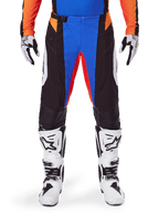 Alpinestars 2025 Techstar Melt Motocross-Hose, Orange und Blau, getragen mit passendem Trikot und weißen Stiefeln, mit schwarzen Einsätzen und leuchtend blauen sowie orangen Akzenten, perforiert für Belüftung, athletische Race-Passform für Offroad-Performance.