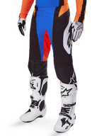 Alpinestars 2025 Techstar Melt Hose, Motocross-Hose, Schwarz mit blauen und orangefarbenen Akzenten, getragen mit weißen Stiefeln und passendem Trikot, mit strapazierfähigem Schutzmaterial und sportlichem Renn-Design