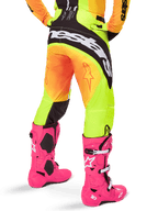 Rückansicht eines Motocross-Fahrers in der Alpinestars 2025 Techstar Melt Hose, gelb-orangefarbener Farbverlauf mit schwarz-weißem Branding am Gesäß, kombiniert mit leuchtend pinken Motocross-Stiefeln, Performance-Offroad-Ausrüstung.