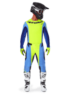 Motocross rider wearing the Alpinestars 2025 Techstar Melt Gear Set, Bright Yellow Fluo jersey with blue and navy sleeves, matching yellow and blue pants, black and white helmet with goggles, white and black boots, yellow and black gloves, coordinated outfit for off-road racing