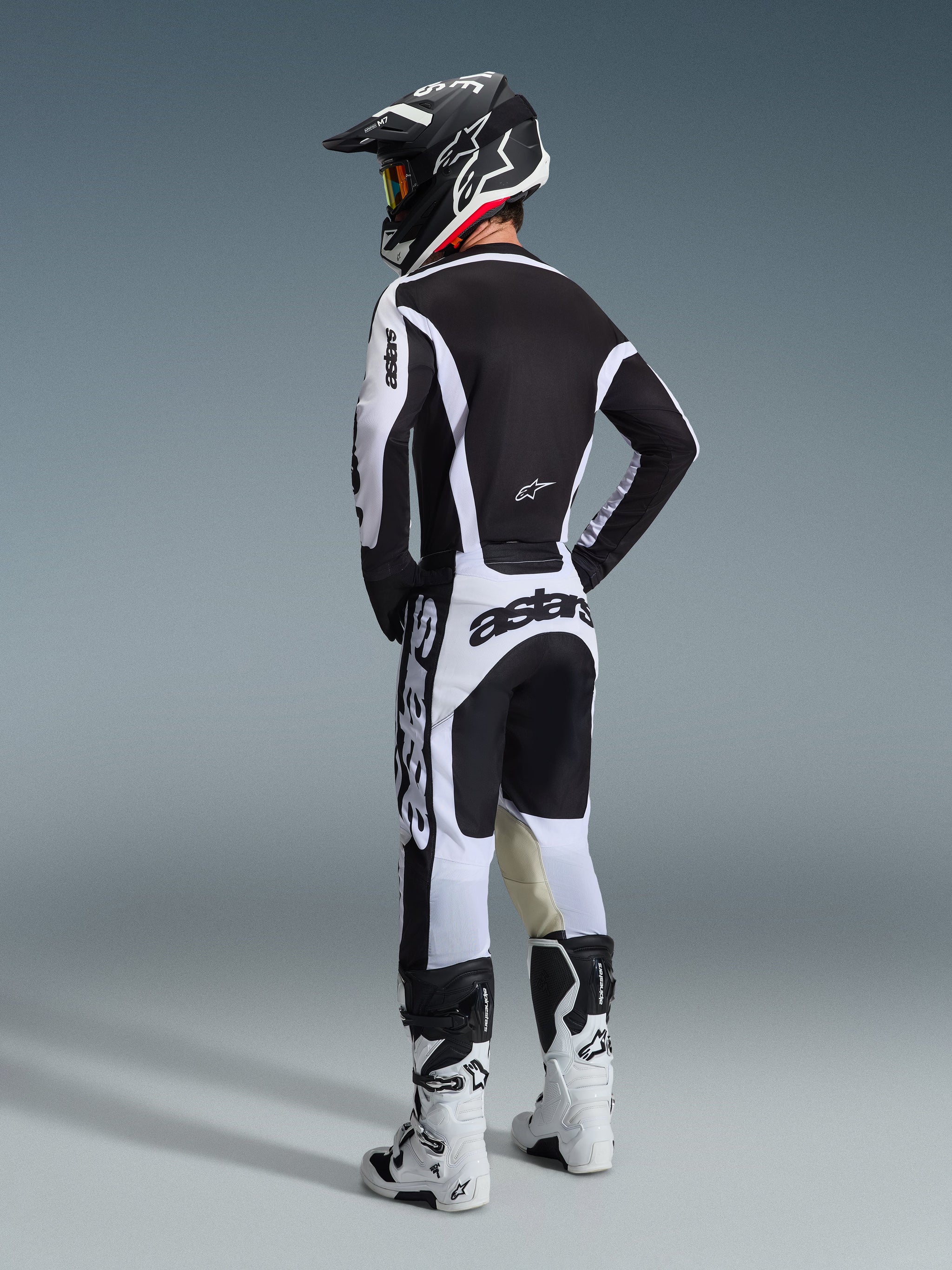 Motocross rider from behind wearing Alpinestars 2026 Racer Riway Pants in White and Black, matching black and white jersey with bold branding, black and white helmet, and white motocross boots, complete racing gear set for off-road performance.