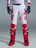 Alpinestars 2026 Racer Riway Hose, Motocross-Hose, Wei&szlig;, Blau und Rot, getragen mit roten Stiefeln und dunkelblauen Handschuhen, mit gro&szlig;en roten Logos auf den Oberschenkeln und roten Knieeins&auml;tzen, sportliches, vorgeformtes Design mit verstellbarer Taillenschnalle