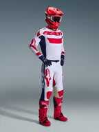 Motocross-Fahrer in kompletter Rennausrüstung, Alpinestars 2026 Racer Riway Hose in Weiß, Blau und Rot, weiße Grundfarbe mit auffälligen roten Logos und blauen Seiteneinsätzen, kombiniert mit passendem weiß-roten Trikot, rotem Helm und roten Motocross-Stiefeln.