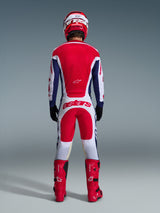 Motocross-Fahrer von hinten in vollständiger Rennausrüstung, Alpinestars 2026 Racer Riway Hose in Weiß, Blau und Rot mit passendem Jersey, roten Stiefeln und Helm, mit großem „astars“-Logo auf der Sitzfläche, koordiniertes Motocross-Outfit.