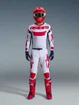 Motocross-Fahrer in kompletter Rennausrüstung, weißes Trikot mit rotem Alpinestars-Branding und blauen Akzenten, Alpinestars 2026 Racer Riway Hose in Weiß-Blau-Rot, roter Helm mit passender Brille, rote und schwarze Stiefel, marineblaue Handschuhe, abgestimmtes Outfit für den Offroad-Rennsport
