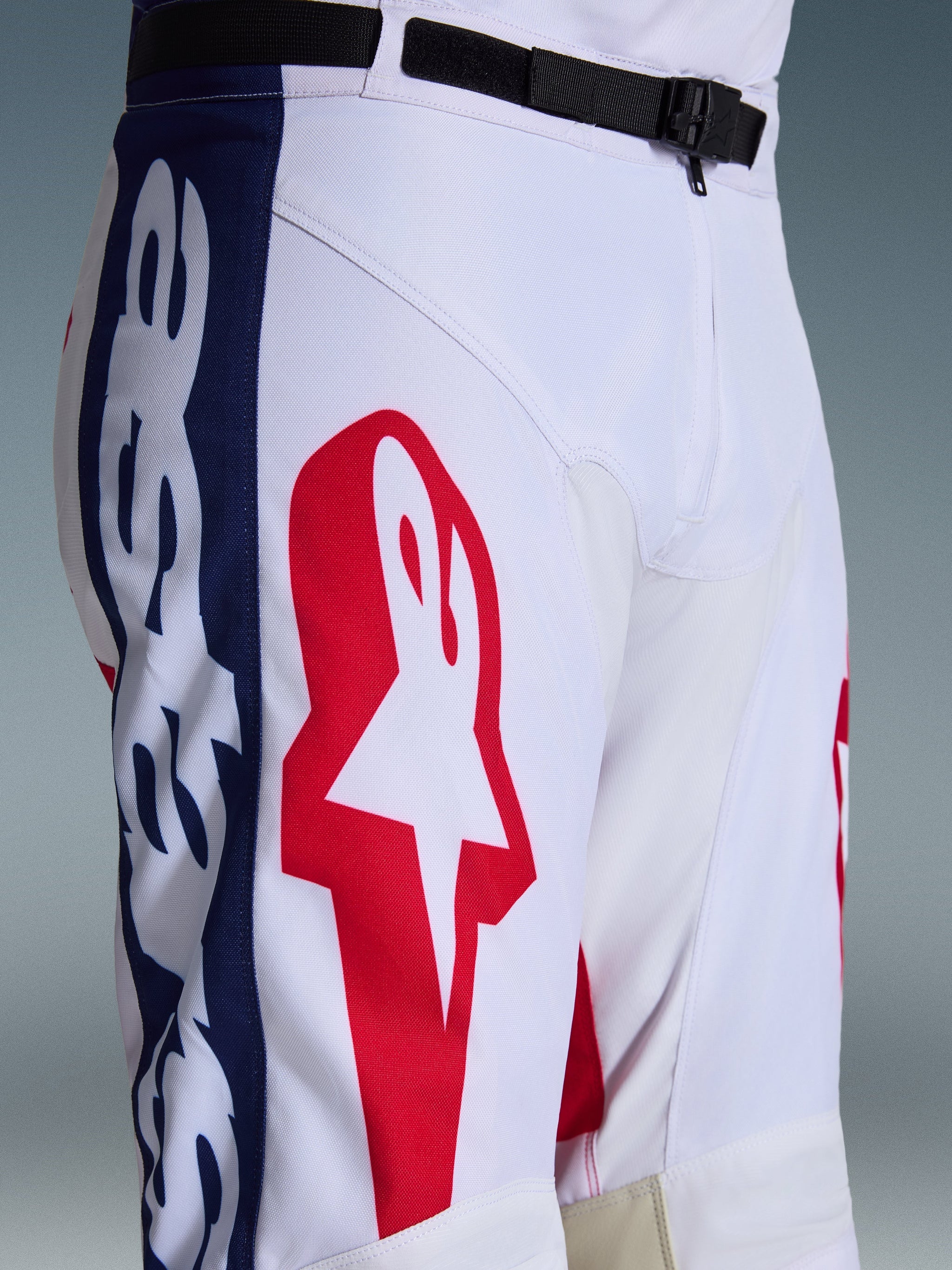 Alpinestars 2026 Racer Riway Hose, Motocross-Hose, Weiß Blau Rot, Nahaufnahme von Oberschenkel und Taille mit großem rotem Stern-Logo auf weißem Polygewebe, blauen Seiteneinsätzen mit Branding und schwarzem verstellbarem Taillengürtel mit SX2-Magnetschnalle, sportliches Offroad-Rennsport-Design