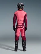 Motocross rider from the back wearing Alpinestars 2026 Racer Riway Pants in Dark Red Coral, matching jersey, black helmet, black gloves, and black Alpinestars boots, featuring a bold 'astars' logo on the seat and a two-tone red design.