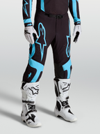 Alpinestars Supertech Vesta Hose, Motocross-Rennsport-Hose für Herren, Schwarz und Türkis, aus Stretch-Ripstop mit Innenkniepanels aus Ziegenleder, getragen mit weißen Tech 10 Stiefeln und Handschuhen.