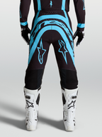 Alpinestars Supertech Vesta Hose, Motocross-Hose in Schwarz und Türkis mit athletischer Passform, getragen mit weißen Offroad-Stiefeln, Pro-Level MX-Bekleidung