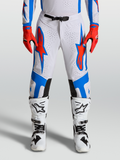 Alpinestars Supertech Vesta Hose, Motocross-Hose in Weiß, Blau und Rot, athletische Passform mit Perforationen, getragen von einem Model mit Handschuhen und Stiefeln für professionelle Offroad-Performance
