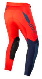 Alpinestars Supertech Blaze Hose, Motocross-Hose, Hellrot und Dunkelblau, Dreiviertelansicht von hinten, mit dunkelblauem ASTARS-Logo an der Seite, schwarzen verstärkten Kniepaneelen und sportlicher Passform für Offroad-Performance.