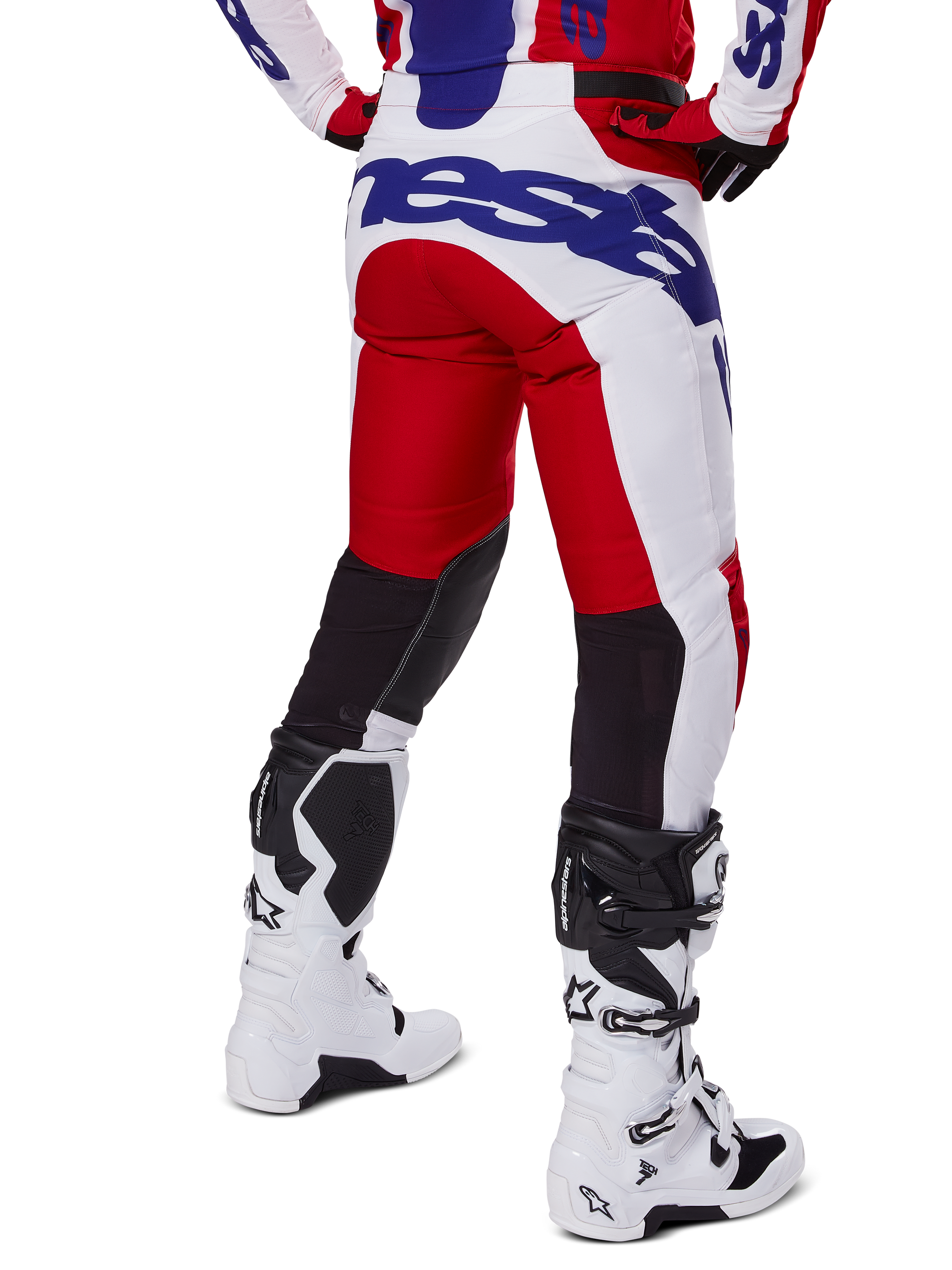 Alpinestars 2025 Racer Veil Hose, Motocross-Hose, Hellrot und Weiß mit blauem Branding, Rückansicht mit schwarzen Stretch-Belüftungseinsätzen an der Beinrückseite, kombiniert mit weißen Motocross-Stiefeln.