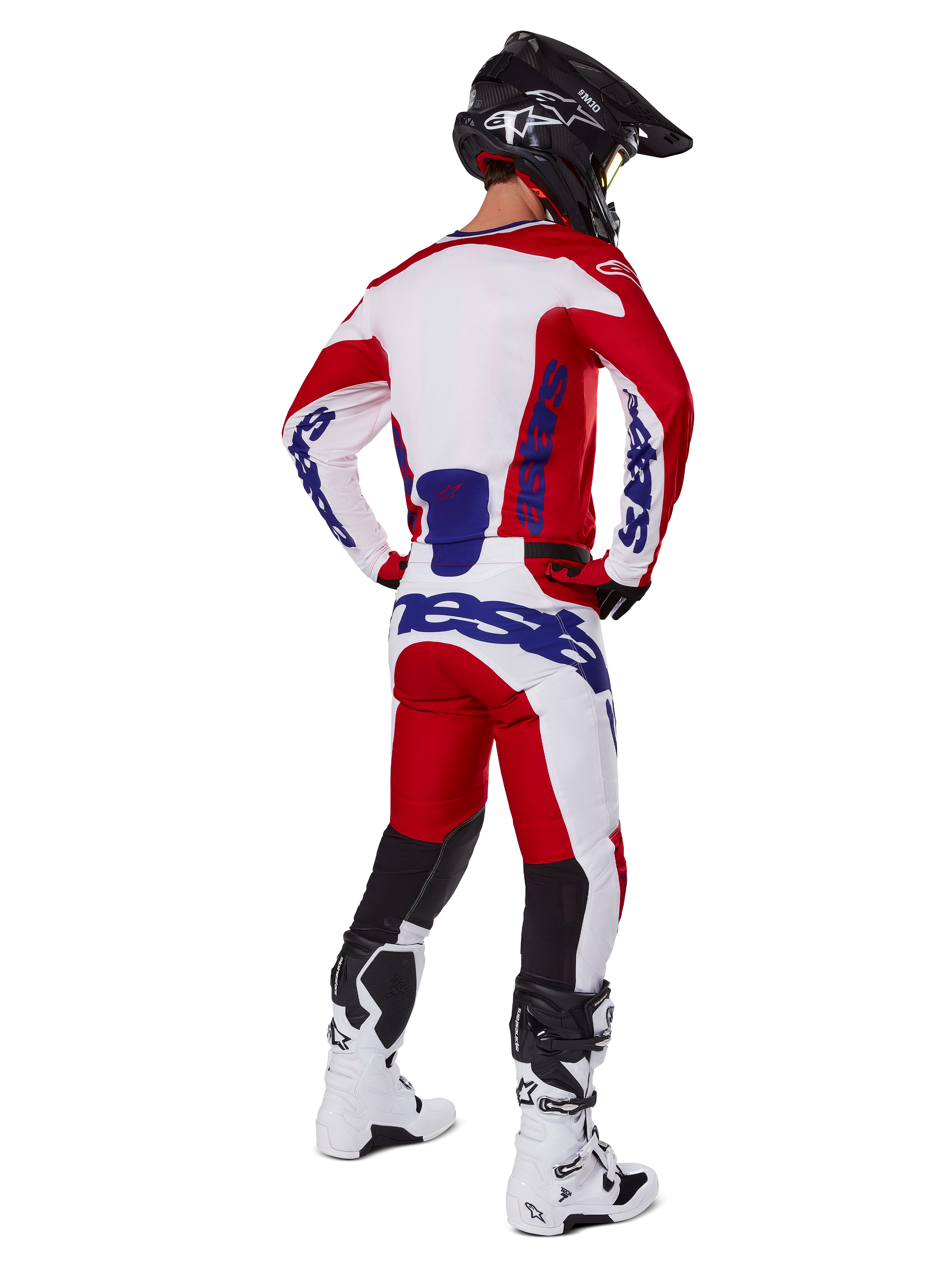 Alpinestars 2025 Racer Veil Hose, Motocross-Hose, Hellrot und Weiß mit blauen Akzenten, Rückansicht eines Fahrers in kompletter Ausrüstung, markantes Alpinestars-Branding, atmungsaktive Einsätze an den Unterschenkeln, dazu passende weiße Stiefel und schwarzer Helm.