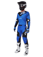 Motocross rider wearing complete racing gear, featuring Alpinestars 2025 Racer Veil Pants in Blue and Black, matching blue jersey with white accents, black helmet with white goggles, white and black boots, and blue gloves, coordinated outfit for off-road racing
