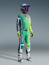 Motocross-Fahrer mit Alpinestars 2026 Racer Portl Hose und passendem Trikot in Grün, Weiß und Schwarz mit pinkfarbenen Logo-Akzenten, bunter Helm, weiß-schwarze Rennstiefel und neongrüne Handschuhe, komplette Ausrüstung für den Offroad-Rennsport