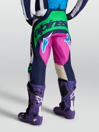Alpinestars Techstar Maven Hose, Motocross-Ausrüstung in Blau, Grün und Pink, Rückansicht am Model mit violetten Tech 10 Stiefeln, strapazierfähige Offroad-Bekleidung.