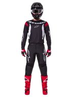 Alpinestars 2025 Fluid Haul Ausrüstungsset, Motocross-Fahrer in kompletter Rennausrüstung, schwarzes Trikot mit roten Schulterakzenten und weißen Logos, schwarze Hose mit weißem Stern-Branding, leuchtend rote Stiefel, rot-schwarze Handschuhe, schwarzer Helm mit weißer Brille, abgestimmter Offroad-Performance-Look