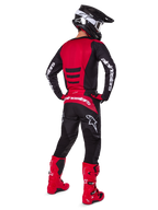 Motocross-Fahrer, der das Alpinestars 2025 Fluid Haul Gear Set in der Rückansicht trägt, rot-schwarzes Jersey mit weißem Branding, passende schwarze Hose mit roten Akzenten, leuchtend rote Stiefel und schwarzer Helm mit weißer Brille, komplett aufeinander abgestimmtes Outfit für Offroad-Rennen