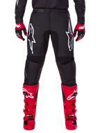 Alpinestars 2025 Fluid Haul Gear Set, schwarze Motocross-Hose mit weißen Astars-Logos auf den Oberschenkeln, kombiniert mit leuchtend roten Stiefeln und rot-schwarzen Handschuhen, abgestimmtes Motocross-Outfit für Offroad-Rennsport