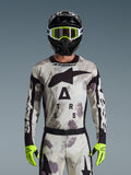 Motocross-Fahrer im Alpinestars 2026 Racer Lahnd Jersey, Sand-Camo-Muster in Grau und Weiß, großes schwarzes Astar-Logo und Branding auf der Brust, kombiniert mit einem schwarzen Helm, neongelber Brille und Handschuhen, Performance-Ausrüstung für Offroad-Fahrten