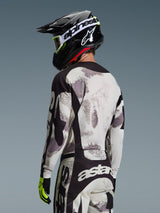 Motocross rider from behind wearing the 2026 Racer Lahnd Jersey in Sand Camo, gray and white abstract patterned jersey with black accents, paired with a black Alpinestars helmet, white goggles, and neon yellow gloves, showcasing the back profile and performance fit for off-road racing.