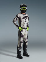 Motocross-Fahrer in kompletter Alpinestars Rennausrüstung, 2026 Racer Lahnd Hose in Sand Camo, passendes Camo-Trikot mit auffälligem Branding, schwarzer Helm mit neongelber Brille, neongrüne Handschuhe und schwarze Stiefel, koordiniertes Profi-Outfit für Offroad-Performance.