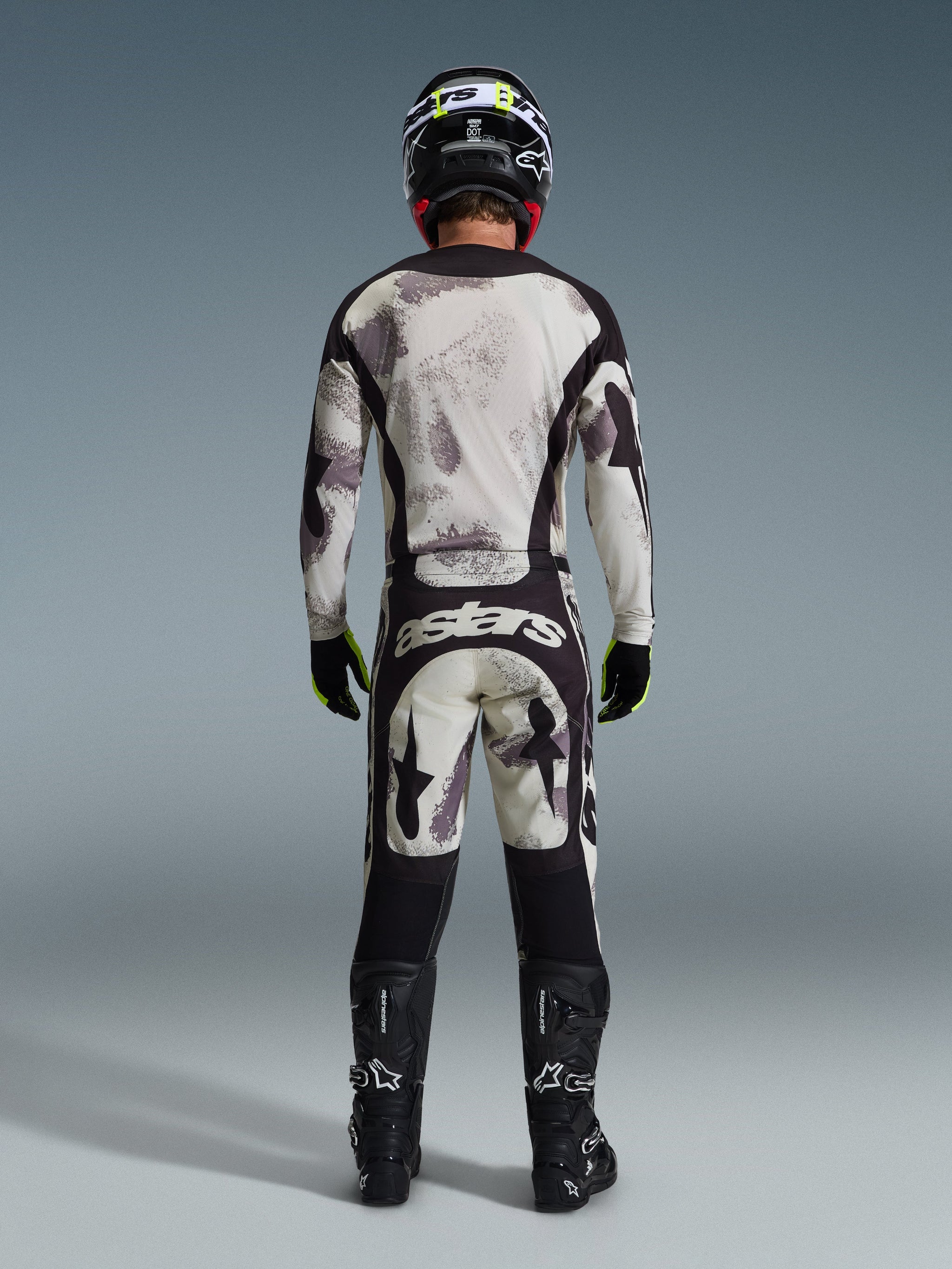 Motocross-Fahrer von hinten in der Alpinestars 2026 Racer Lahnd Hose in Sand Camo, passendes Langarm-Trikot mit grauem Camouflage-Muster, schwarze Motocross-Stiefel, schwarzer Helm und „astars“-Branding am Gesäß, entwickelt für professionellen Offroad-Rennsport.