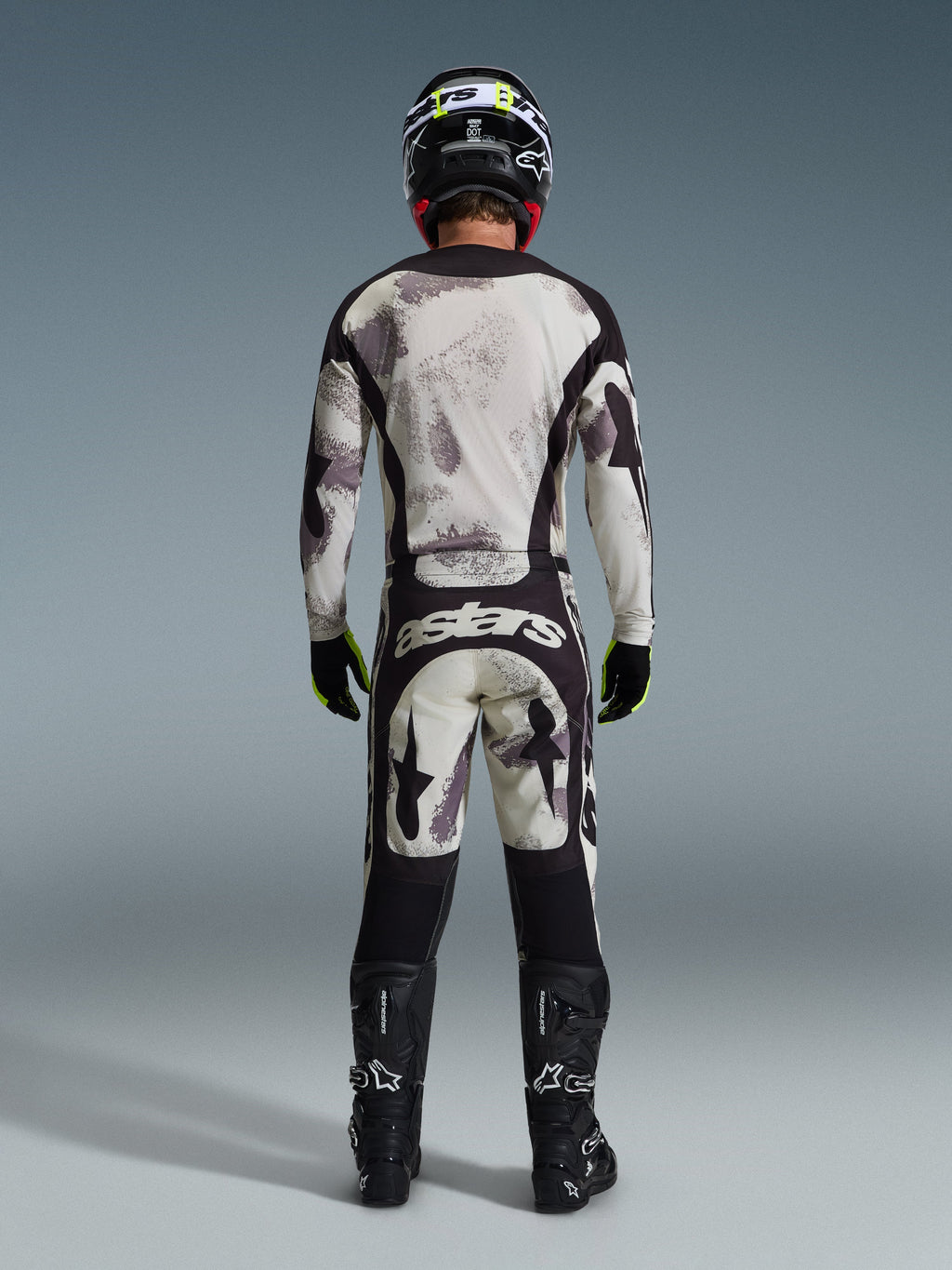 Motocross-Fahrer von hinten im 2026 Racer Lahnd Trikot und der passenden Hose in Sand Camo, mit einem abstrakten Muster in Creme und Grau sowie schwarzen Einsätzen, „astars“-Branding auf der Hose, kombiniert mit schwarzen Alpinestars-Stiefeln und einem schwarzen Helm für einen kompletten Offroad-Rennlook.