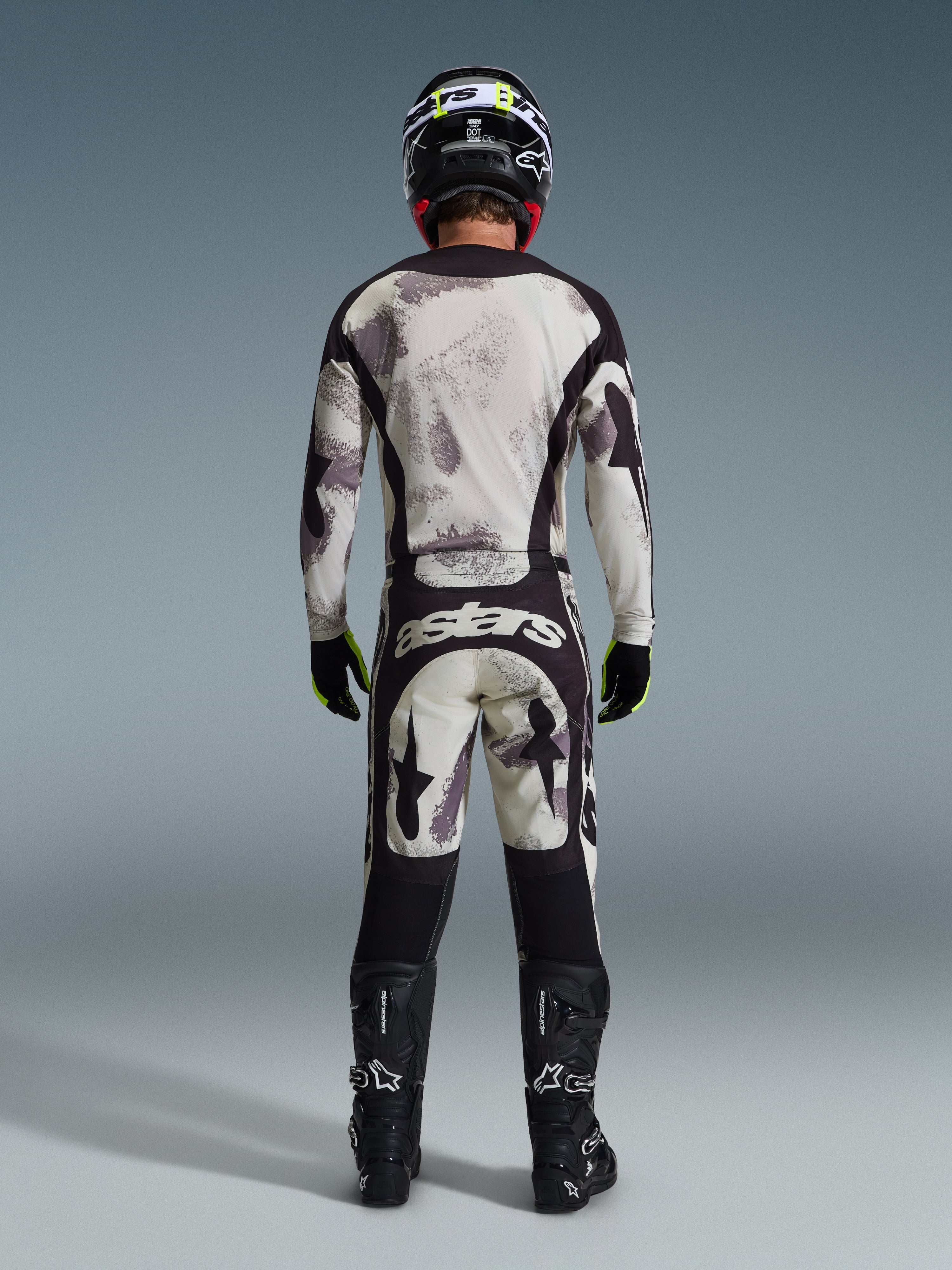 Motocross-Fahrer von hinten im 2026 Racer Lahnd Trikot und der passenden Hose in Sand Camo, mit einem abstrakten Muster in Creme und Grau sowie schwarzen Einsätzen, „astars“-Branding auf der Hose, kombiniert mit schwarzen Alpinestars-Stiefeln und einem schwarzen Helm für einen kompletten Offroad-Rennlook.